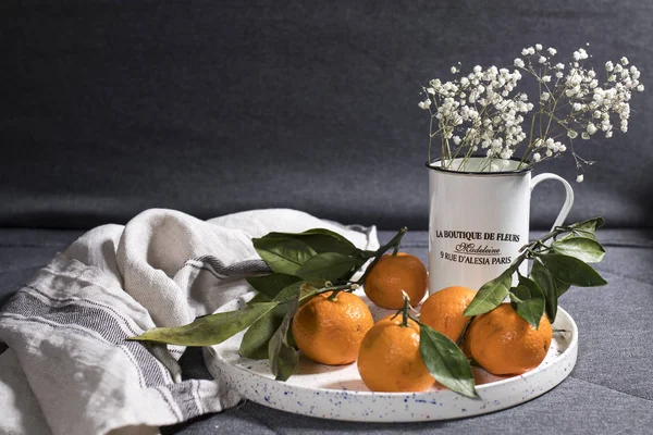 Tangerines met groene bladeren op witte keramische schaal met een grijze keukendoek — Stockfoto