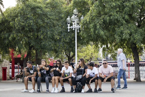 Большая семья сидит на длинной скамейке и ест мороженое в порту — стоковое фото