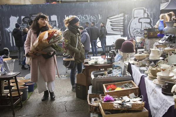 Une fille en fausse fourrure passe devant un comptoir avec de vieilles choses vendues dans un marché aux puces — Photo