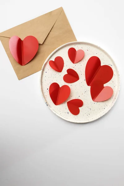 Corazones de plástico rojo en un plato de cerámica blanca. Tarjeta de San Valentín — Foto de Stock