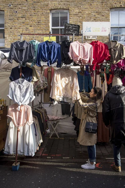 Bezoekers kijken naar kleding op de Brick Lane straat markt. Meisje en jongen kijken naar de modieuze multi-gekleurde jassen Pilot. — Stockfoto