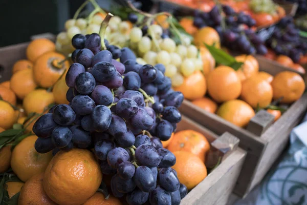 Białe i niebieskie winogrona na tle mandarynek i pomarańczy na ladzie w Borough Market. Wnętrze sklepu warzywnego — Zdjęcie stockowe