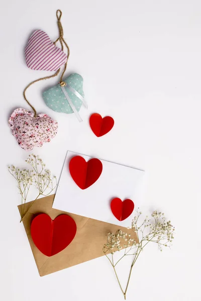 Tarjeta de felicitación para el día de San Valentín. Sobres sobre fondo blanco y corazones rojos de plástico . — Foto de Stock