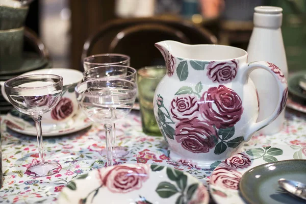 White ceramic plates on a shelf in a store. Designer ceramic plates with a pattern. tableware and eating concept. White jug with roses for table setting with glasses for wine and a bottle for water.