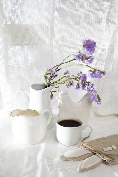 Festive table decoration for Easter. Coffee, milk jug and a bouquet of blue flowers in a jug, as well as a bag with a gift in the shape of an Easter hare.