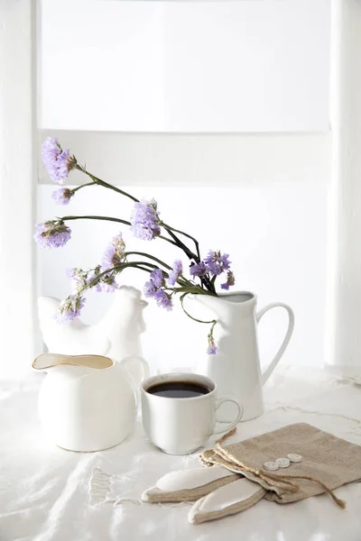 Festive table decoration for Easter. Coffee, milk jug and a bouquet of blue flowers in a jug, as well as a bag with a gift in the shape of an Easter hare.