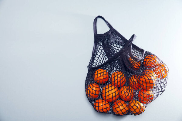 Blue string bag with tangerines on a blue paper background