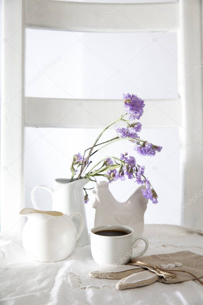 Festive table decoration for Easter. Coffee, milk jug and a bouquet of blue flowers in a jug, as well as a bag with a gift in the shape of an Easter hare.