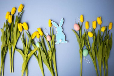 Sarı lale buketi, paskalya tavşanı ve mavi arka planda yumurtalar. Uzayı kopyala Tasarımcı kartı.