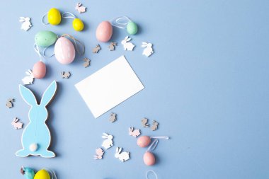 Mavi arka planda plastik yumurta ve kartla mavi tahta düz paskalya tavşanı. Boşluğu kopyala