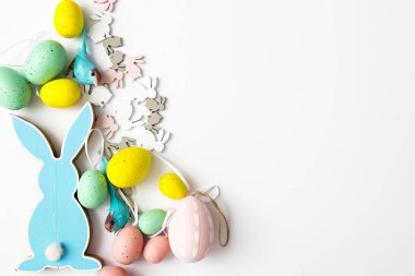 Beyaz arka planda, üzerinde plastik yumurtalar olan mavi, düz bir Paskalya tavşanı yatıyor. Boşluğu kopyala