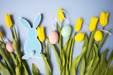 Sarı lale buketi, paskalya tavşanı ve mavi arka planda yumurtalar. Uzayı kopyala Tasarımcı kartı.