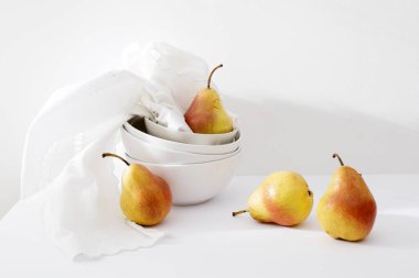 Beyaz duvarda beyaz işlemeli bir peçete ve çanak çömlek içinde sarı-kırmızı armut düşesi ile hayat. Boşluğu kopyala