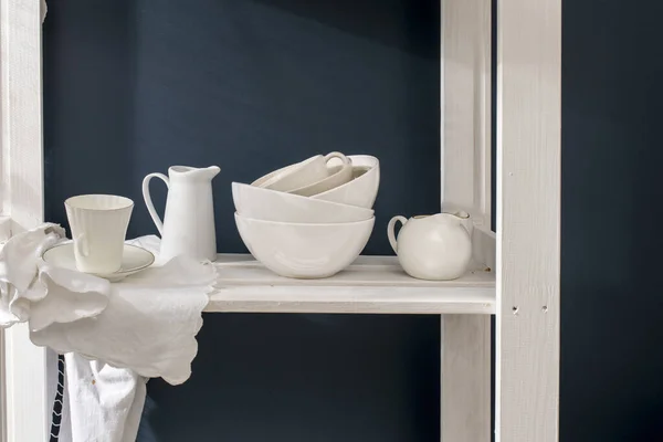 一套白色的盘子 瓷质牛奶壶 咖啡杯 放在深蓝色背景的白色架子上的碗 — 图库照片