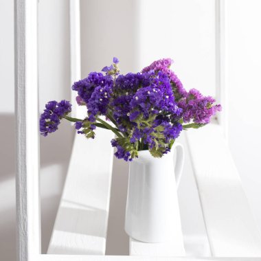 Beyaz bir rafta taze limonyum bulunan beyaz toprak sürahisi..