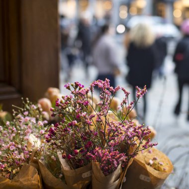 Balmumu çiçeği buketi bej el sanatları kağıdına sarılı, sokak arkaplanının karşısındaki mağazada satılık.