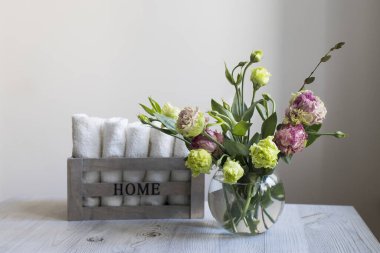 Yeşil ve pembe terry lisianthus buketi ve şeffaf yuvarlak bir vazoda okaliptüs dalları. Gelin buketi. Tahta kutuda beyaz Terry tekstil el havluları ve ahşap masa üzerinde 