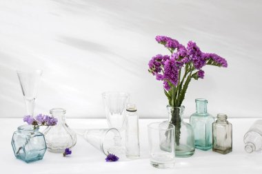 Şeffaf vazoda bir buket limonyum ve beyaz arka planda küçük şişeler..