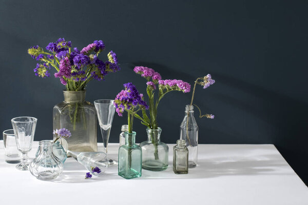 A bouquet of limonium in the transparent vase and a set of small bottles on a dark blue background.