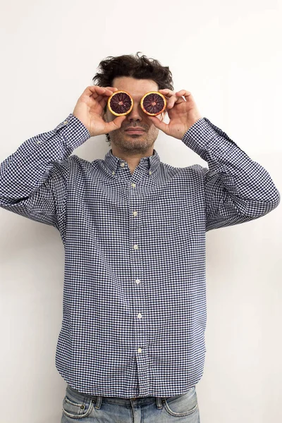 funny curly man in a plaid shirt put two halves of a red orange to his eyes. Funny picture