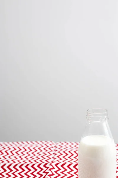 An open bottle of milk is on a red and white tablecloth in a zigzag on the table against the background of a gray wall in the kitchen. Copy space