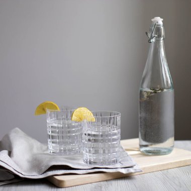 Limonata ve şeffaf şişe içinde limonata gri duvarın arka planında. Limon dilimli iki kıvrımlı bardak. Gri peçete ve kesme tahtası. Uzayı kopyala Açık renkli resim