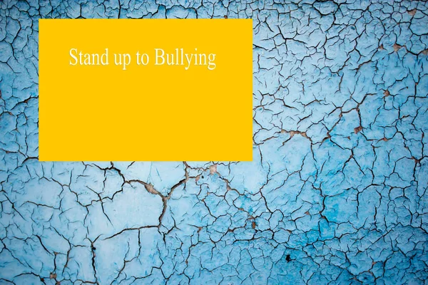 Old peeling blue paint on a concrete wall of a house. Yellow blank with text - Stand Up to Bullying