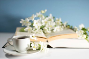 Çiçek açan bir elma ağacının dalı ya da açık bir kitap üzerinde kiraz ağacı ve mavi bir duvarın arka planında bir fincan kahve. Kavram - çevrimiçi öğrenme. Uzayı kopyala Eğitim çevrimiçi