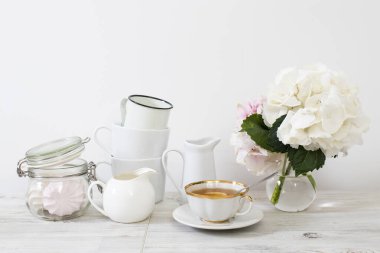 Yuvarlak cam bir vazoda top şeklinde beyaz ortanca, bir dizi hafif tabak, süt sürahisi, porselen ve emaye kaplar, beyaz arka planda bir tebrik kartı için bir sürahi..