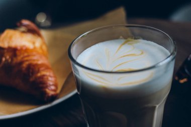 Karanlık retro ahşap arka plan üzerinde kruvasan ile latte cam fincan. 