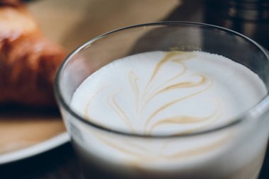 Karanlık retro ahşap arka plan üzerinde kruvasan ile latte cam fincan. 