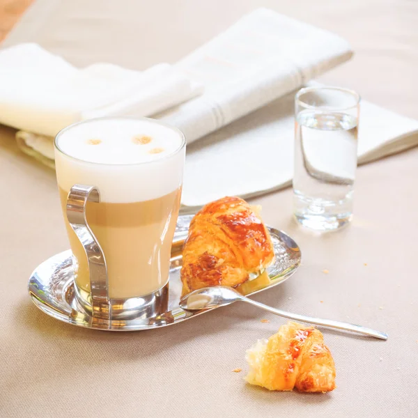 Cup of latte with croissant. Tablecloth background with newspape — Stockfoto