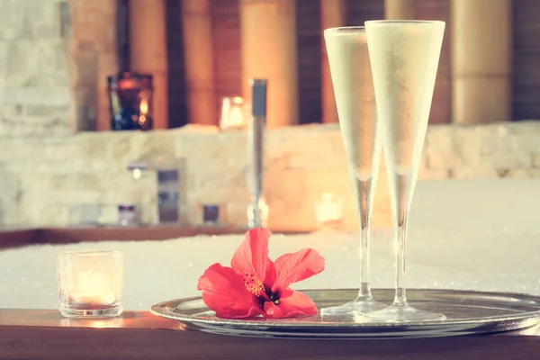 Dos copas de champán con vela y flor roja cerca de jacuzzi — Foto de Stock