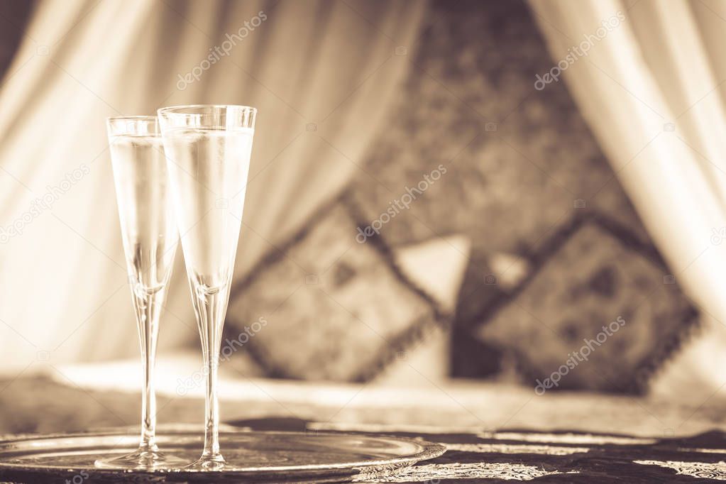 Two champagne glasses with oriental canopy bed at the background