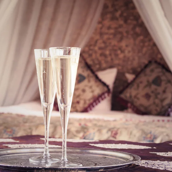 Two champagne glasses with oriental canopy bed at the background — Stock Photo, Image