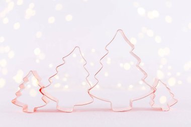 Family of Christmas Tree Copper cookie cutter on white sparkling background with bokeh lights. Holiday Christmas and New Year background