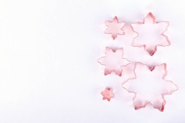 Beyaz ışıl ışıl arka planda çeşitli kar taneli bakır kurabiye kalıpları olan düz bir yatak. Tatil, Noel ve Yeni Yıl konsepti. Samimi ev detayları