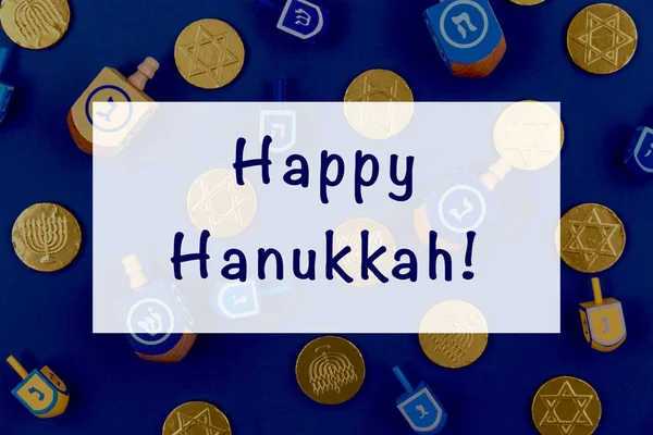 Fondo azul oscuro con dreidels multicolores y monedas de chocolate y la redacción feliz Hanukkah. Hanukkah y judaic concepto de vacaciones . — Foto de Stock