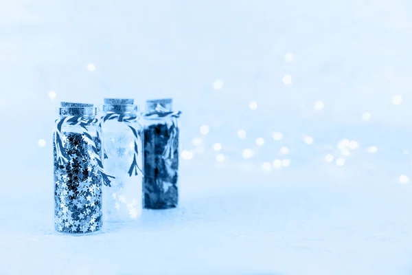 Γυάλινα μπουκάλια με glitter κομφετί σε λευκό φόντο με bokeh φώτα. Διακοπές Χριστούγεννα και Πρωτοχρονιά φόντο τονισμένο σε κλασικό μπλε — Φωτογραφία Αρχείου