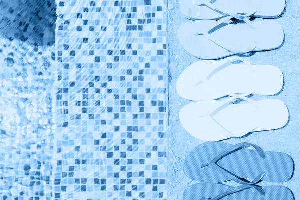 Ряд шлепанцев возле бассейна, тонированный в классическом синем — стоковое фото