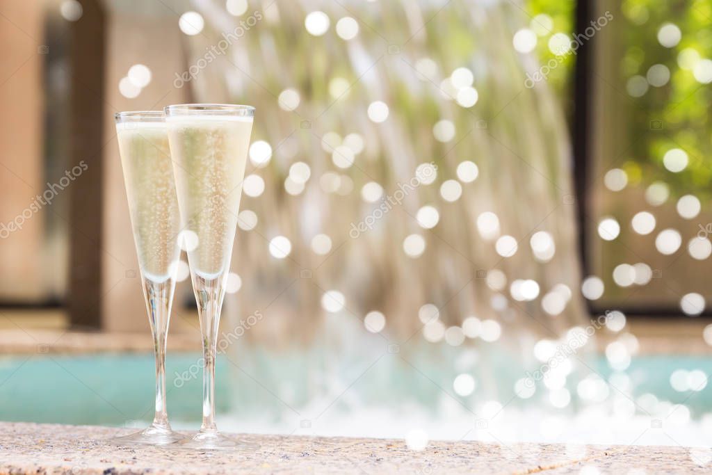 Two glasses of champagne near outdoor jacuzzi with gentle festive holiday bokeh
