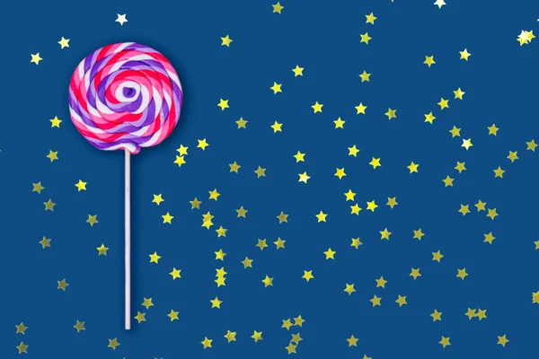 Большой леденец на твердом классическом синем фоне с праздничными конфетти в форме золотой звезды — стоковое фото