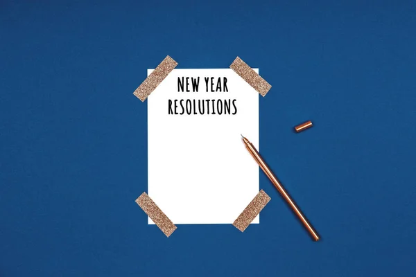 Clean and stylish isolated white card with New Year resolutions wording and golden pen. Flat lay background in gold and classic blue colors for any celebration and party occasion — Stock Photo, Image