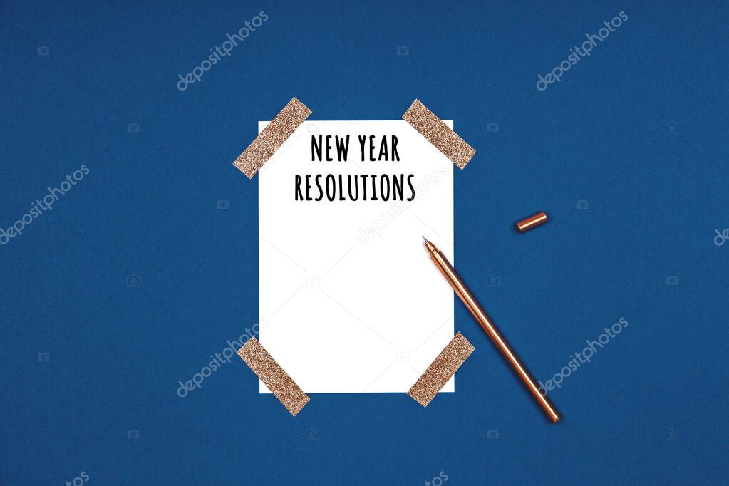 Clean and stylish isolated white card with New Year resolutions wording and golden pen. Flat lay background in gold and classic blue colors for any celebration and party occasion