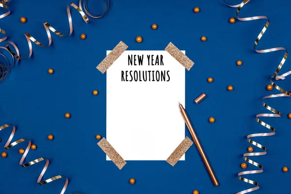 White card with New Year resolutions wording and golden pen with festive golden ribbons and confetti. Flat lay background in gold and classic blue colors for any celebration and party occasion — Stock Photo, Image