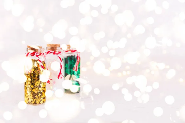 Botellas de vidrio con confeti de brillo sobre fondo blanco con luces bokeh. Navidad y Año Nuevo fondo con luces festivas bokeh — Foto de Stock