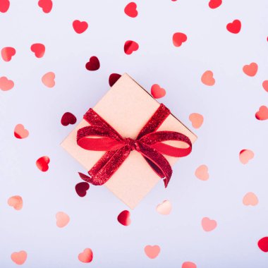 Kırmızı kurdele yayı ve parıltılı kalp konfetisi olan el işi kutusu. Sevgililer Günü ve çevre dostu paket konsepti. Moda minimalist düz dizayn arkaplanı