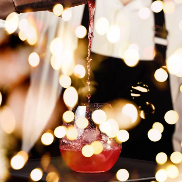 Barman in making cocktail at a nightclub. Nightlife concept. No face. Pouring into glass with festive bokeh lights — Stock Photo, Image