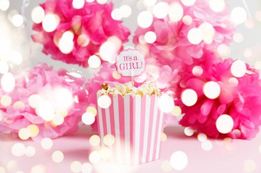 Its a girl sign in a popcorn bag at the baby shower party. Paper flowers background. Baby shower celebration concept with festive holiday bokeh clipart