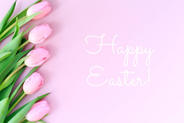 Happy Easter wording with pink tulips on the pink background. Flat lay, top view